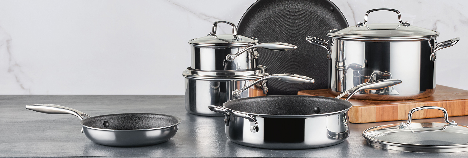 A set of shiny stainless steel pots and pans with lids, arranged on a kitchen counter.