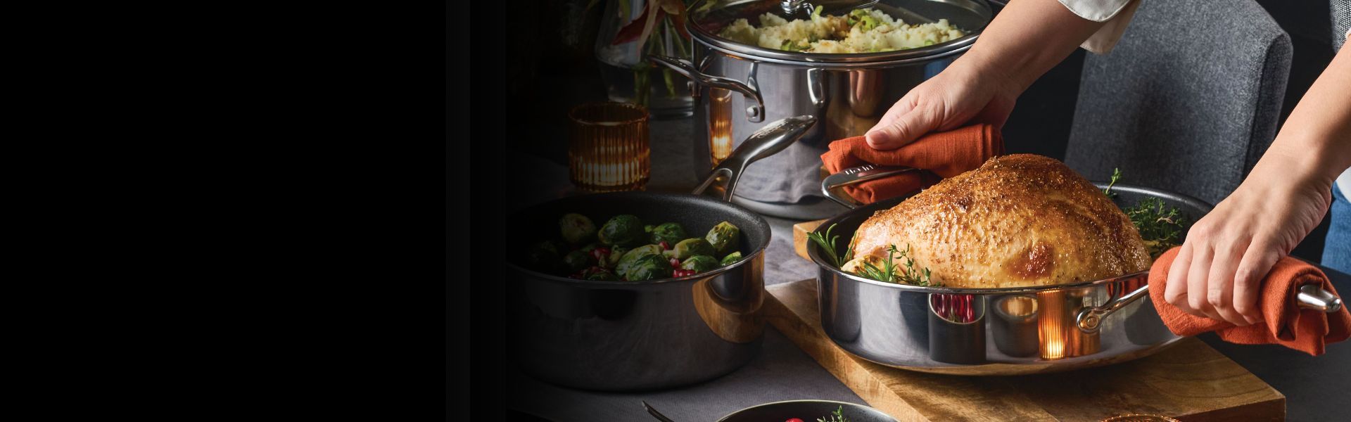 A kitchen scene featuring a set of stainless steel cookware on a stove. One pan is cooking scallops, another contains vegetables. A halved lemon lies nearby.