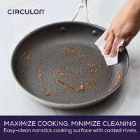 Hand wiping a nonstick pan with a cloth over a marble surface.