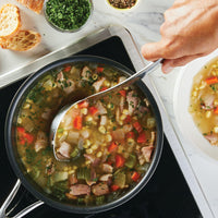 Using the 6-Piece Tool and Crock Set with ergonomic handles, a person stirs a pot of vegetable and meat soup on the stove.