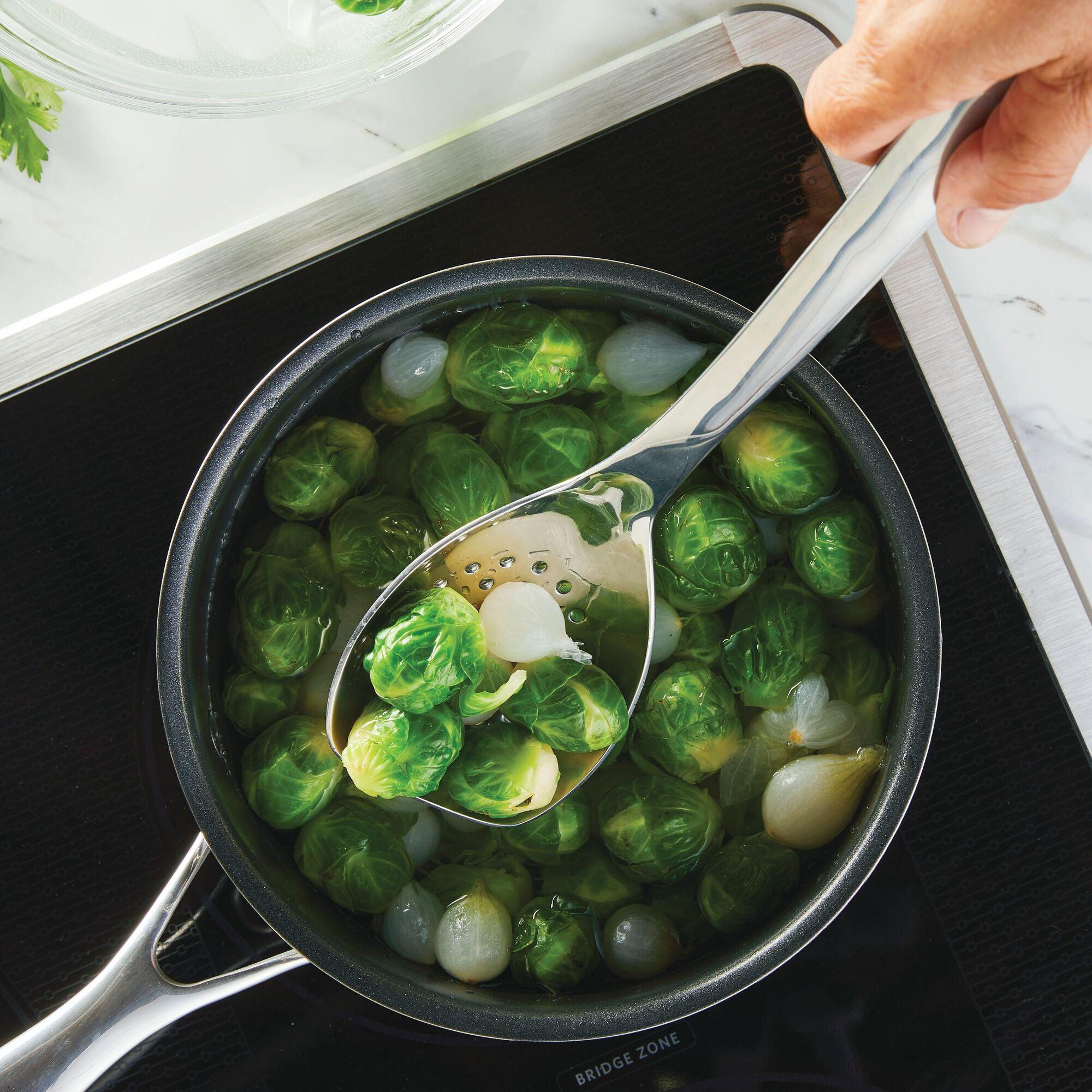 Brussels sprouts and onions simmer in the pot, stirred with a tool from the 6-Piece Tool and Crock Set. The slotted spoon has ergonomic handles, making cooking a breeze. Plus, it's dishwasher safe for easy cleanup!