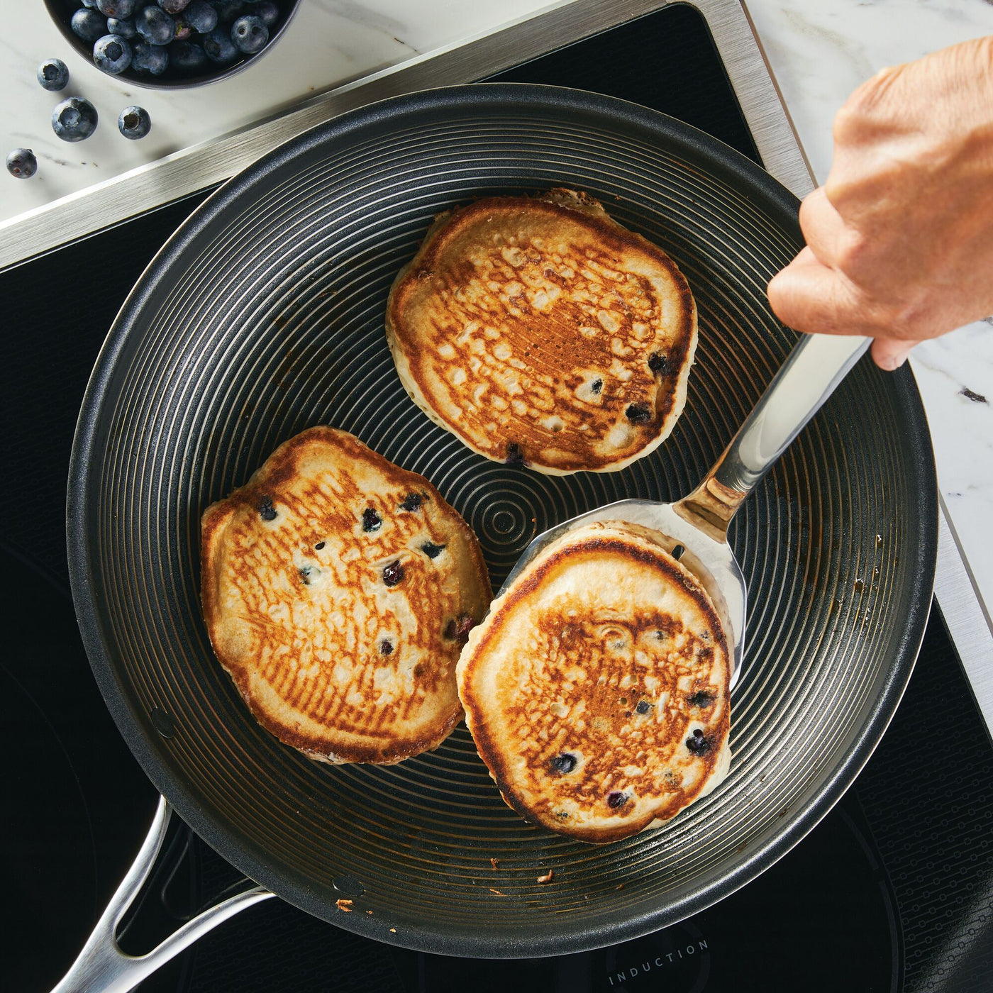 Three blueberry pancakes sizzle in a frying pan on the stove, surrounded by the 3-Piece Kitchen Utensils Set with ergonomic handles, ready for effortless flipping.