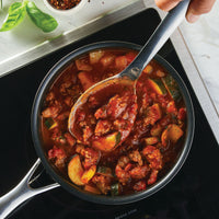 A pot of vegetable and meat stew is being stirred with a ladle from the 6-Piece Tool and Crock Set on a stove, its ergonomic handle offering a comfortable grip for the task.