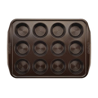 A heavy-duty dark metal muffin baking pan from the 10-Piece Nonstick Bakeware Set, with a 12-cup capacity and circular patterns, made of heavy gauge steel for excellent warp resistance and a nonstick finish.
