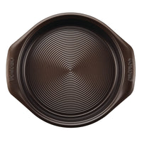The round dark baking pan, part of the 10-Piece Nonstick Bakeware Set, includes a ridged surface with ergonomic handles and is crafted from heavy gauge steel to resist warping.