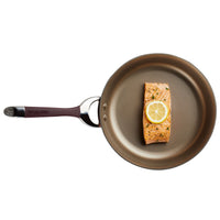 A salmon fillet with a lemon slice sizzles in a Hard-Anodized Frying Pan Set, renowned for its nonstick system, on a white background.